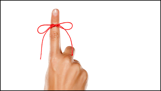 hand with index finger pointing up with red yarn tied in a bow around it. 