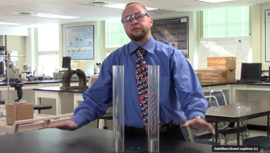 professor in a science lab with 2 tall clear cylinders in front of him